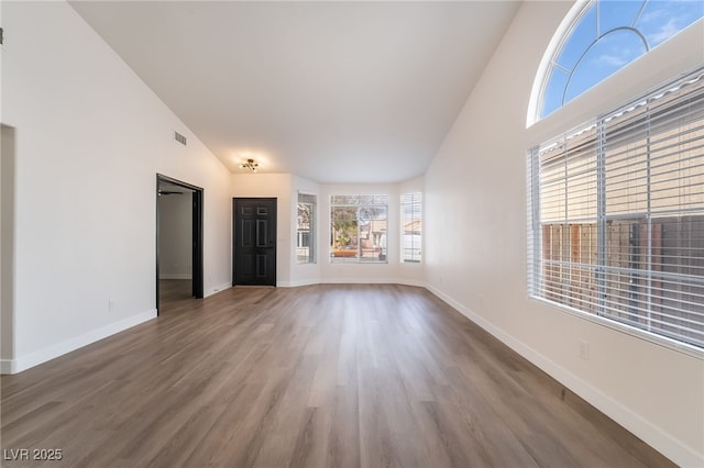 unfurnished living room featuring visible vents, wood finished floors, baseboards, and high vaulted ceiling