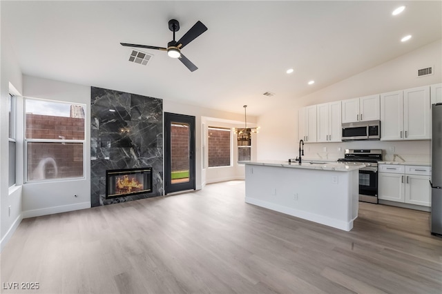 kitchen with visible vents, a fireplace, a sink, vaulted ceiling, and appliances with stainless steel finishes