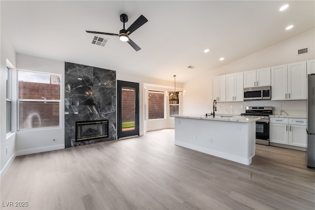 kitchen with visible vents, lofted ceiling, a high end fireplace, a sink, and appliances with stainless steel finishes