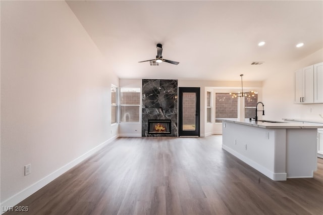 unfurnished living room with a high end fireplace, visible vents, ceiling fan with notable chandelier, wood finished floors, and a sink