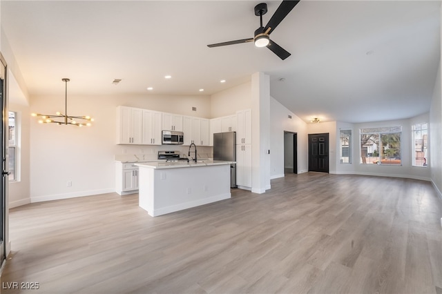 kitchen with a sink, open floor plan, appliances with stainless steel finishes, white cabinets, and light countertops