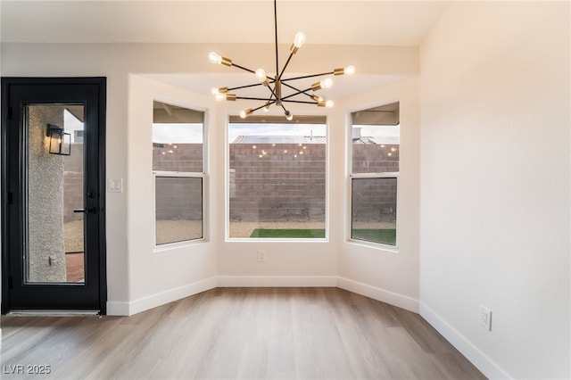 unfurnished dining area with a chandelier, baseboards, and wood finished floors