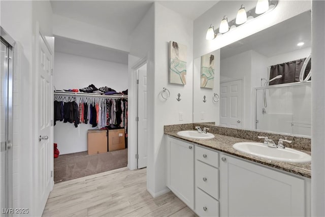 full bath with a sink, wood finished floors, a stall shower, and a spacious closet