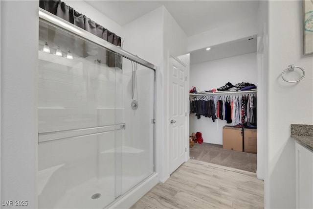 full bath featuring wood finished floors, vanity, a stall shower, and a spacious closet