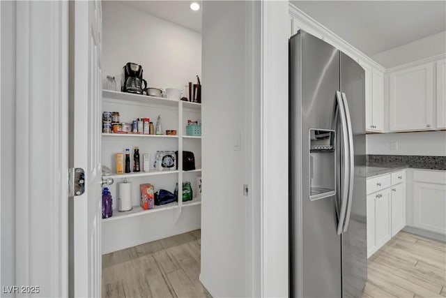 kitchen with stone counters, stainless steel fridge, white cabinetry, and light wood finished floors