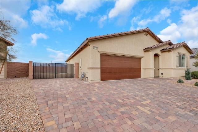 view of side of home with stucco siding, decorative driveway, a garage, and a gate