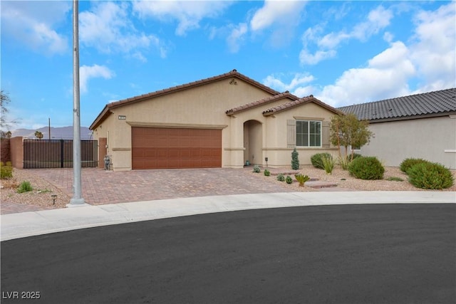 mediterranean / spanish house featuring fence, stucco siding, a garage, a tiled roof, and decorative driveway