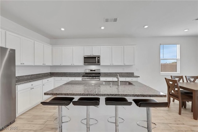 kitchen with visible vents, a breakfast bar, a sink, stainless steel appliances, and white cabinets