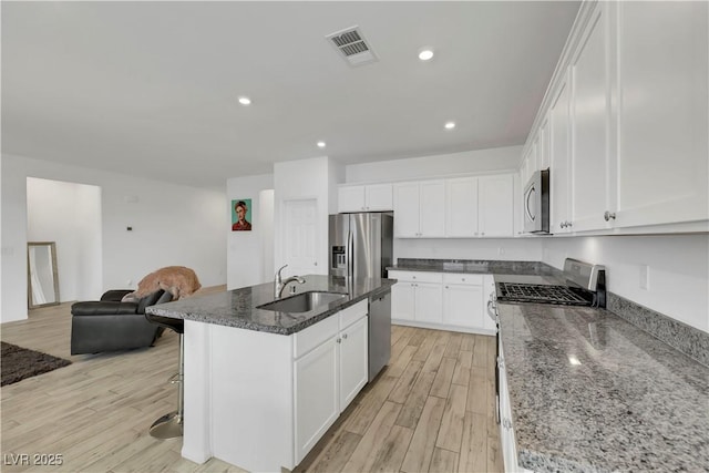 kitchen featuring light wood finished floors, visible vents, open floor plan, stainless steel appliances, and a sink