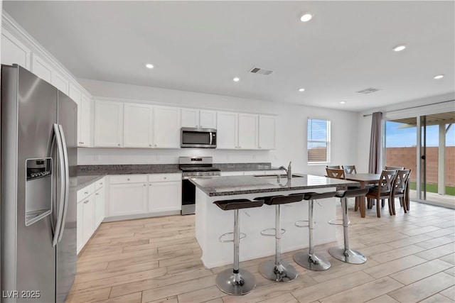 kitchen with a breakfast bar, light wood-style flooring, a sink, white cabinetry, and stainless steel appliances