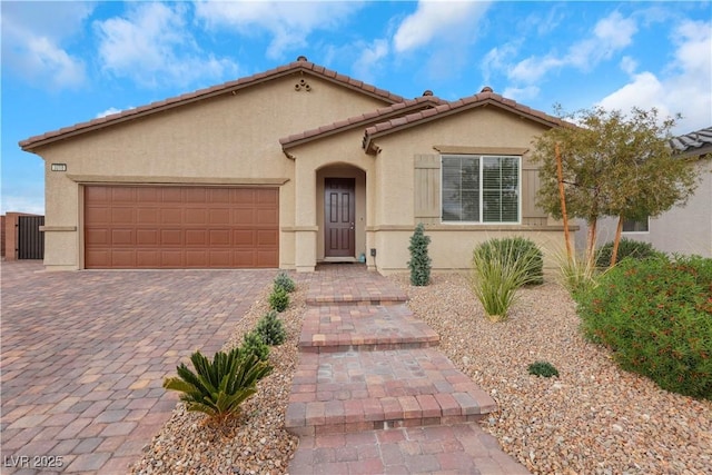 mediterranean / spanish-style home with a tiled roof, decorative driveway, an attached garage, and stucco siding