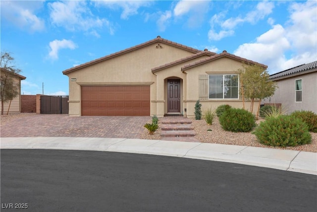 mediterranean / spanish-style home with fence, stucco siding, decorative driveway, a garage, and a gate