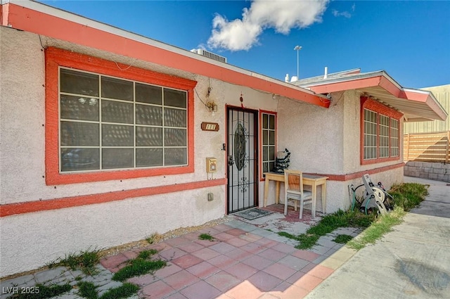 doorway to property with stucco siding and fence