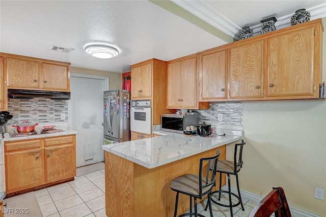 kitchen with visible vents, under cabinet range hood, light tile patterned floors, appliances with stainless steel finishes, and a peninsula