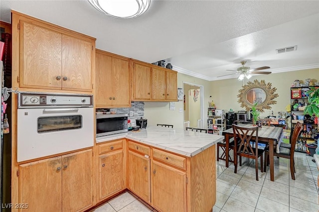 kitchen featuring stainless steel microwave, visible vents, a peninsula, light tile patterned flooring, and white oven