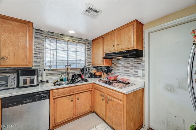 kitchen featuring visible vents, under cabinet range hood, light countertops, stainless steel appliances, and a sink