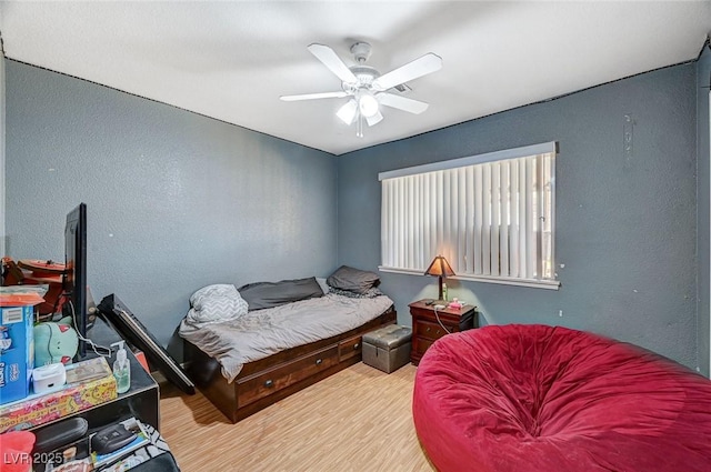 bedroom with wood finished floors, a textured wall, and ceiling fan