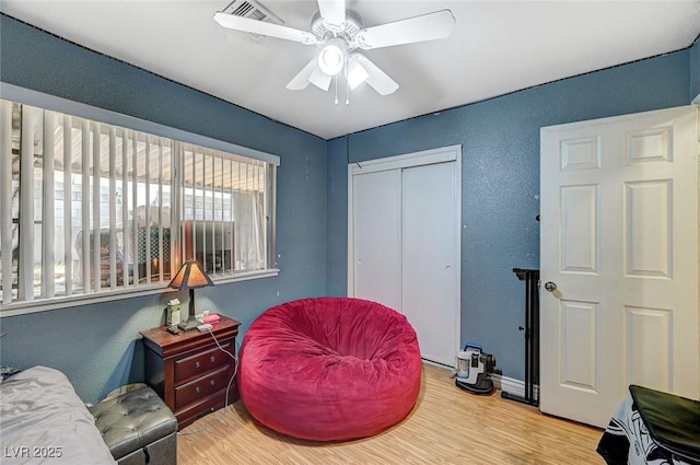 living area featuring a ceiling fan, wood finished floors, visible vents, and a textured wall