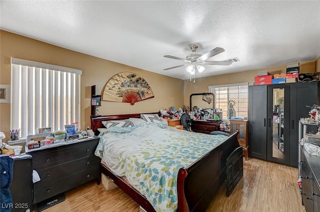 bedroom featuring a ceiling fan, visible vents, light wood finished floors, and a textured ceiling