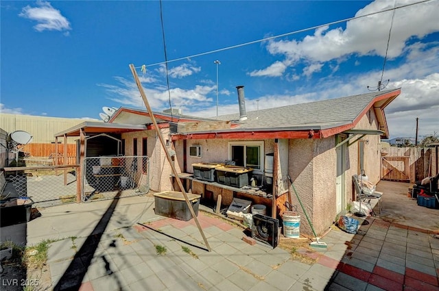 rear view of property featuring stucco siding, a gate, fence, a shingled roof, and a patio area