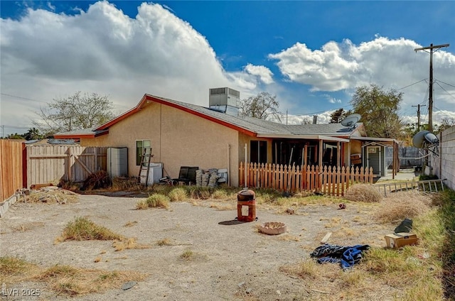 rear view of house featuring stucco siding, fence private yard, and central AC