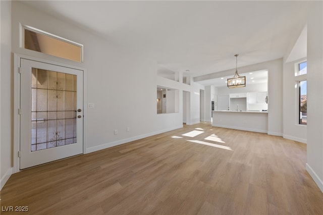 unfurnished living room featuring an inviting chandelier, baseboards, and light wood-type flooring