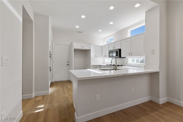 kitchen featuring stainless steel microwave, light countertops, light wood-style flooring, a peninsula, and white cabinetry