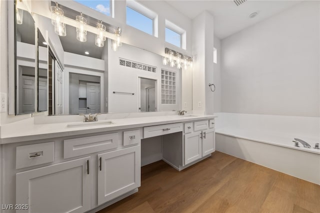 full bath featuring double vanity, wood finished floors, a garden tub, and a sink