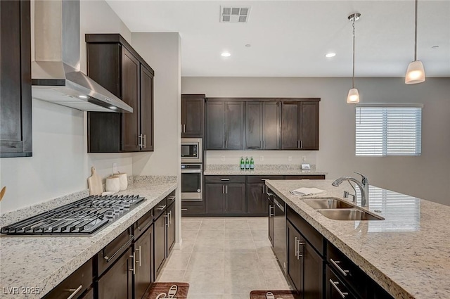 kitchen featuring visible vents, pendant lighting, stainless steel appliances, wall chimney exhaust hood, and a sink