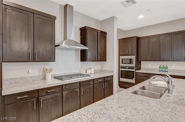 kitchen featuring visible vents, wall chimney range hood, dark brown cabinetry, appliances with stainless steel finishes, and a sink