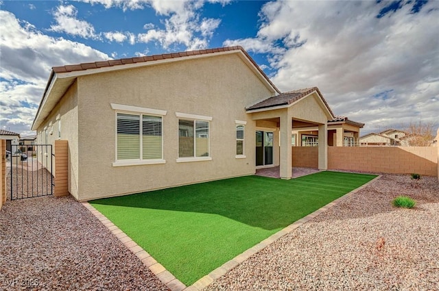 rear view of property featuring a gate, stucco siding, a lawn, and fence