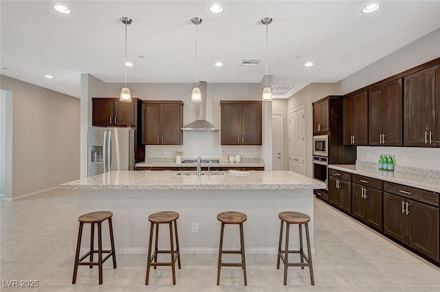 kitchen with visible vents, a kitchen island with sink, a sink, stainless steel appliances, and wall chimney range hood