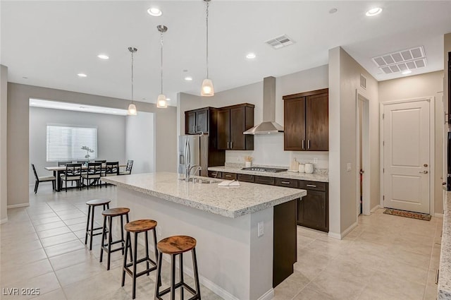 kitchen featuring visible vents, a kitchen bar, wall chimney exhaust hood, and stainless steel appliances