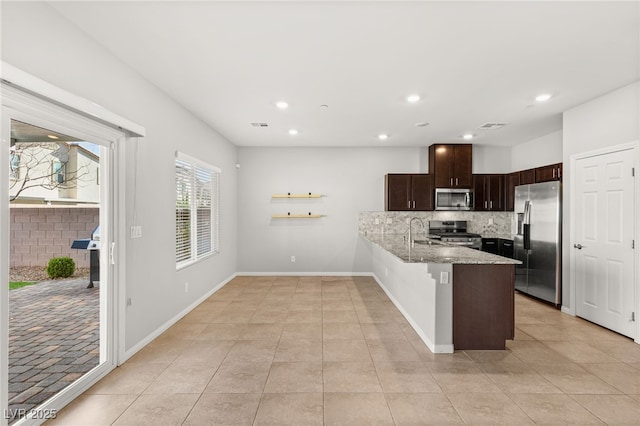 kitchen with light stone counters, stainless steel appliances, dark brown cabinetry, a peninsula, and decorative backsplash