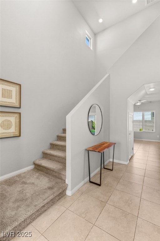 stairway featuring tile patterned floors, baseboards, and a towering ceiling