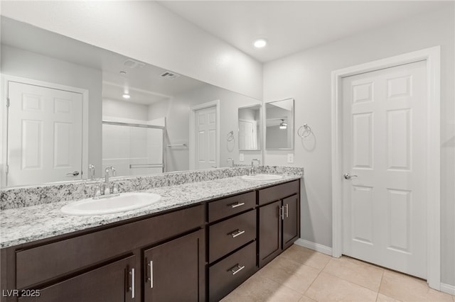 full bath featuring a sink, a shower stall, double vanity, and tile patterned flooring