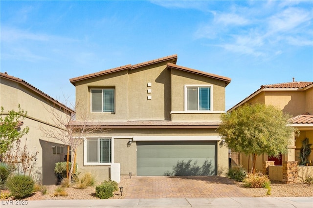 rear view of property featuring stucco siding, decorative driveway, and a garage