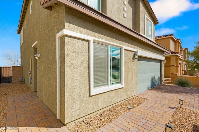 view of side of property with stucco siding, a patio area, an attached garage, and fence