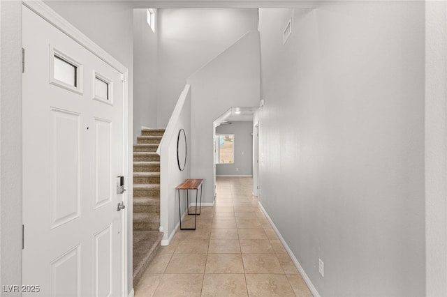 hallway with stairway, arched walkways, light tile patterned floors, baseboards, and a towering ceiling