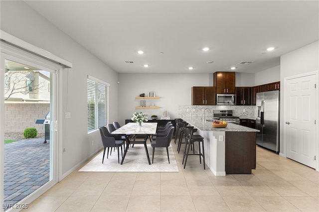 kitchen featuring tasteful backsplash, visible vents, dark brown cabinets, light stone counters, and stainless steel appliances