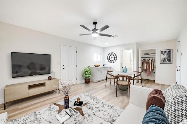 living area with light wood-type flooring, visible vents, baseboards, and a ceiling fan