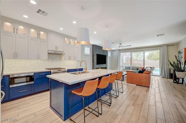 kitchen with visible vents, a sink, under cabinet range hood, blue cabinets, and open floor plan