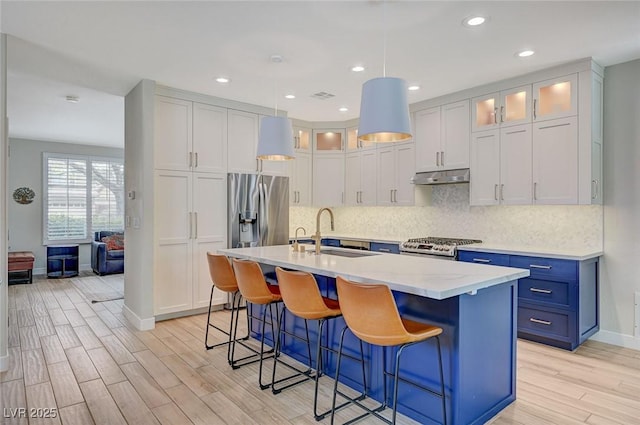 kitchen featuring under cabinet range hood, a sink, range with gas stovetop, stainless steel fridge, and light wood finished floors