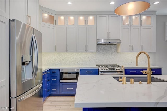 kitchen with under cabinet range hood, decorative backsplash, stainless steel appliances, and blue cabinets