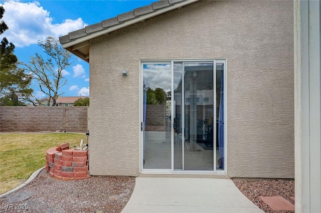 view of exterior entry with a patio, a yard, fence, and stucco siding