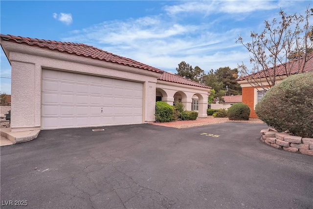 mediterranean / spanish home featuring aphalt driveway, a tiled roof, an attached garage, and stucco siding