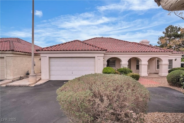 mediterranean / spanish house featuring a tile roof, aphalt driveway, a garage, and stucco siding