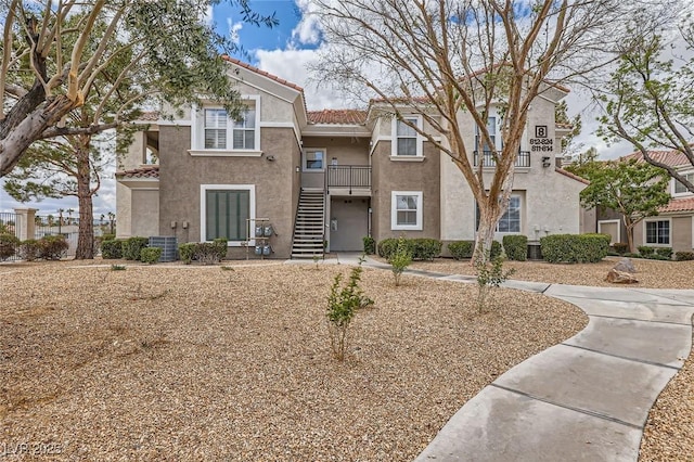 townhome / multi-family property featuring stucco siding, central AC unit, a tile roof, and stairway