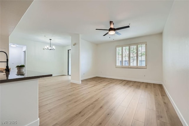 unfurnished living room featuring light wood finished floors, ceiling fan with notable chandelier, baseboards, and a sink