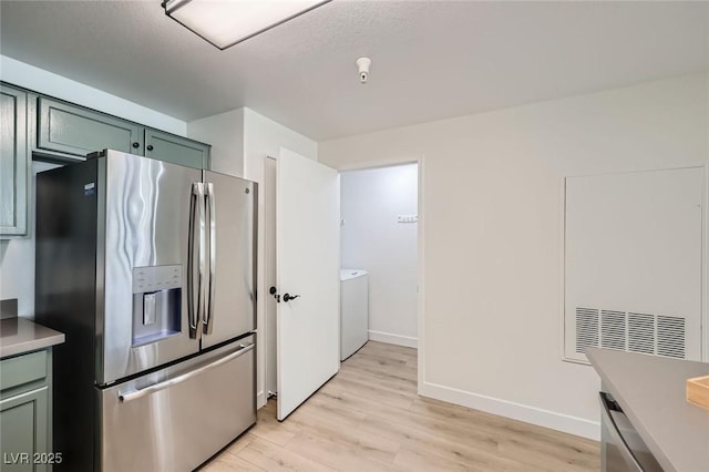 kitchen with washer and dryer, light wood-type flooring, stainless steel fridge, and light countertops